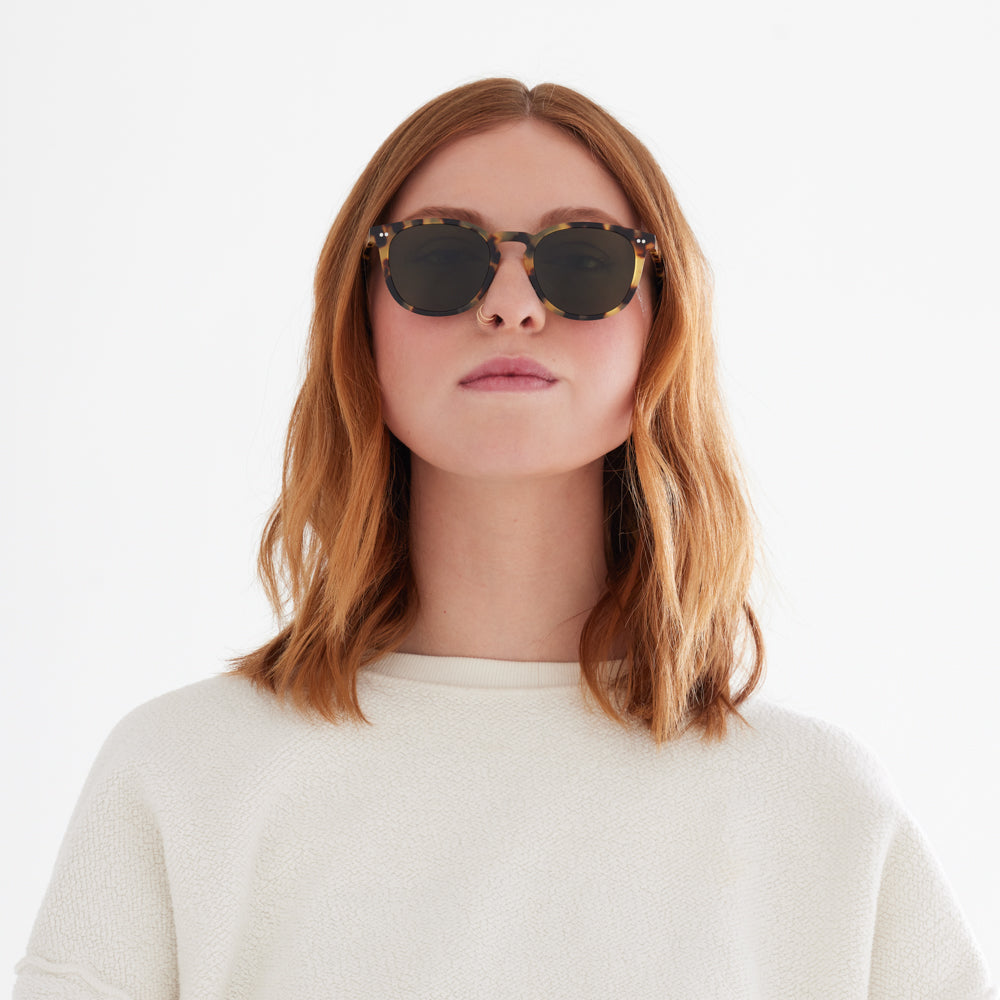 Woman with short red hair wearing the Oak sunglass in tortoise. A round shape sunglass